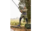 Man fishing in outdoor gear, wearing a two-tone jacket and cargo pants, with a cooler bag.