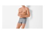 Man in grey boxer briefs leaning against a white wall.
