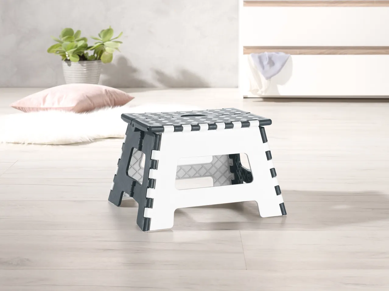 Sgabello pieghevole bianco e grigio con puntini, su pavimento di legno chiaro.