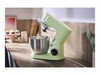 Light green stand mixer with a stainless steel bowl and whisk, containing batter, on a wooden kitchen counter.