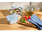 Stainless steel food containers with salad, olive oil, tomatoes, and basil on a wooden board.