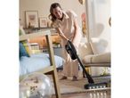 Woman vacuuming a living room with a cordless vacuum cleaner.