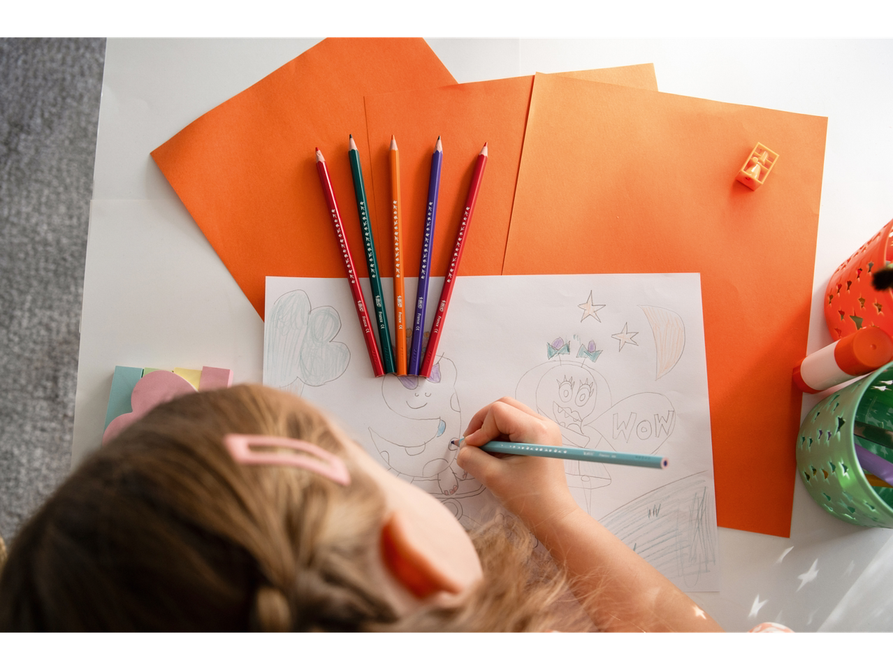 O fetiță desenează cu creioane colorate BIC pe o masă.