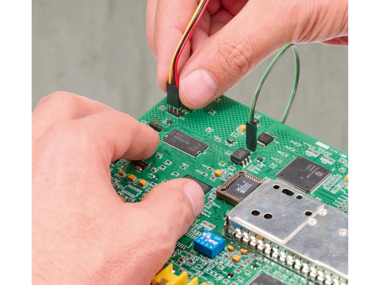 Ruke povezuju žice sa zelenom štampanom pločom sa mikročipovima i komponentama.