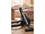 Aspirador Silvercrest® num chão de madeira com uma sala de estar acolhedora ao fundo