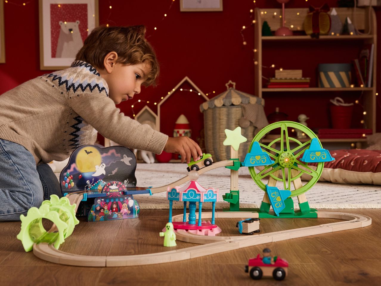 A child plays with a wooden train set featuring a haunted carnival theme.