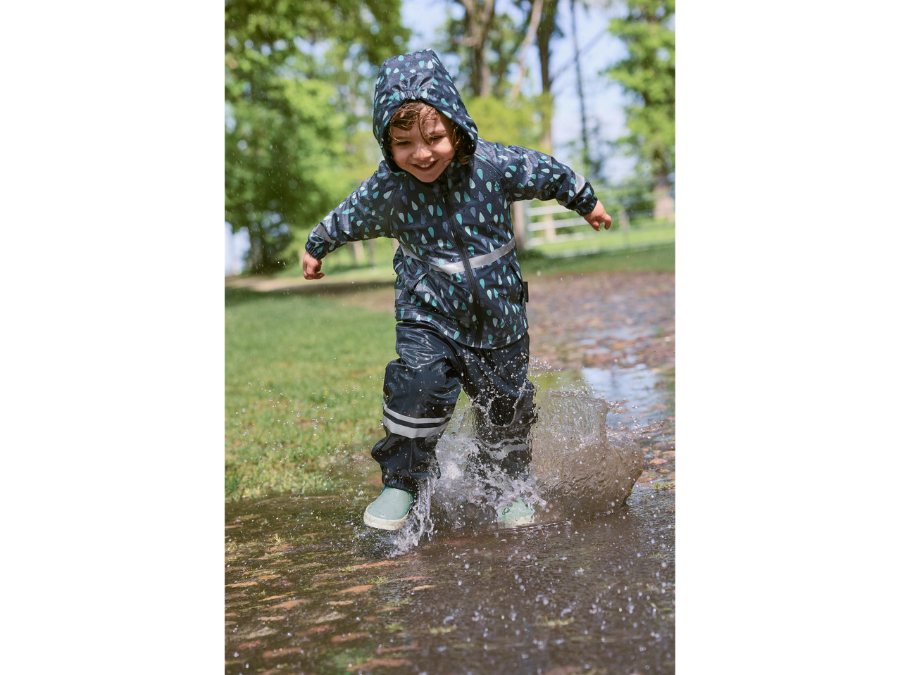 Happy child in a rain suit and boots playing in a puddle.