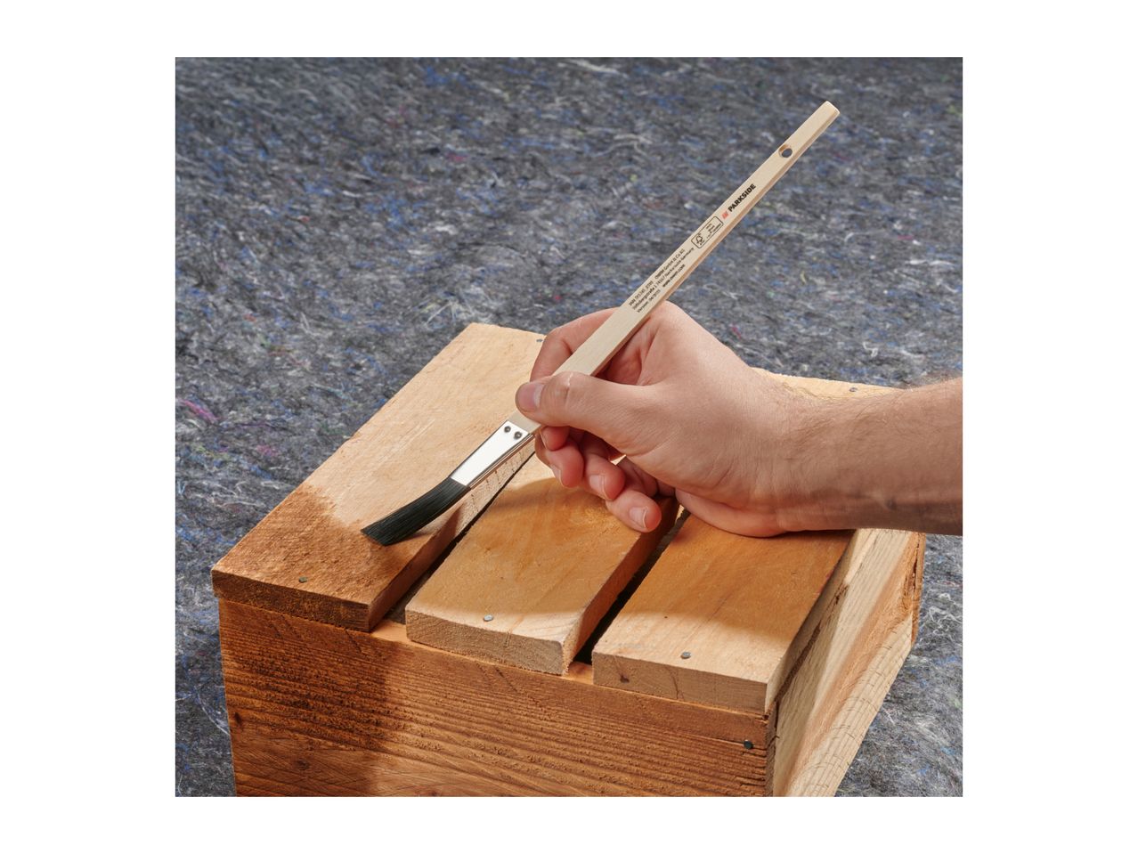 Hand applying wood stain to wooden planks with a brush.