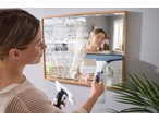Woman cleaning a mirror with a spray bottle and a window vacuum cleaner.