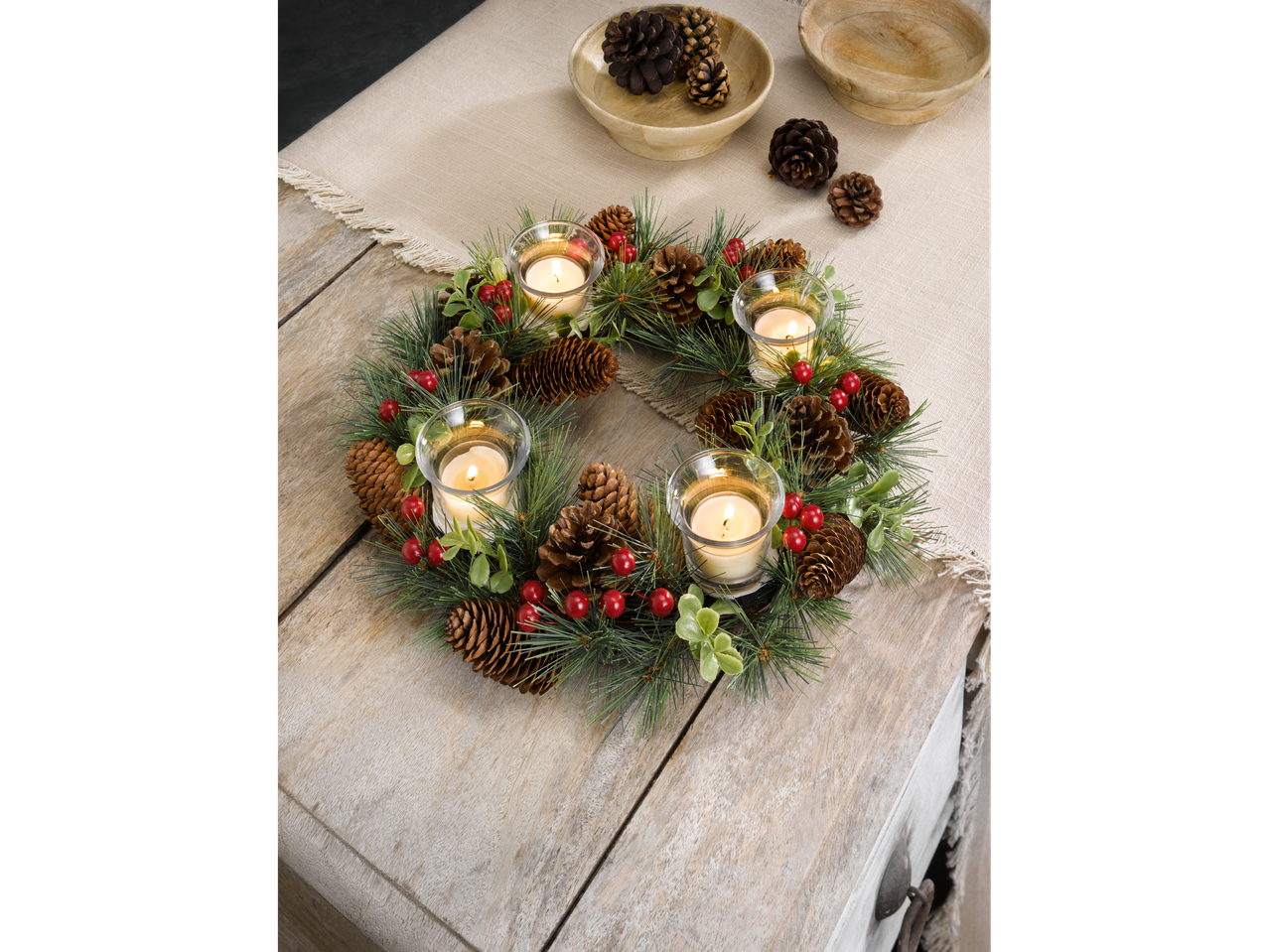 LIVARNO home Christmas Wreath with pinecones, red berries, and four lit candles on a wooden table.