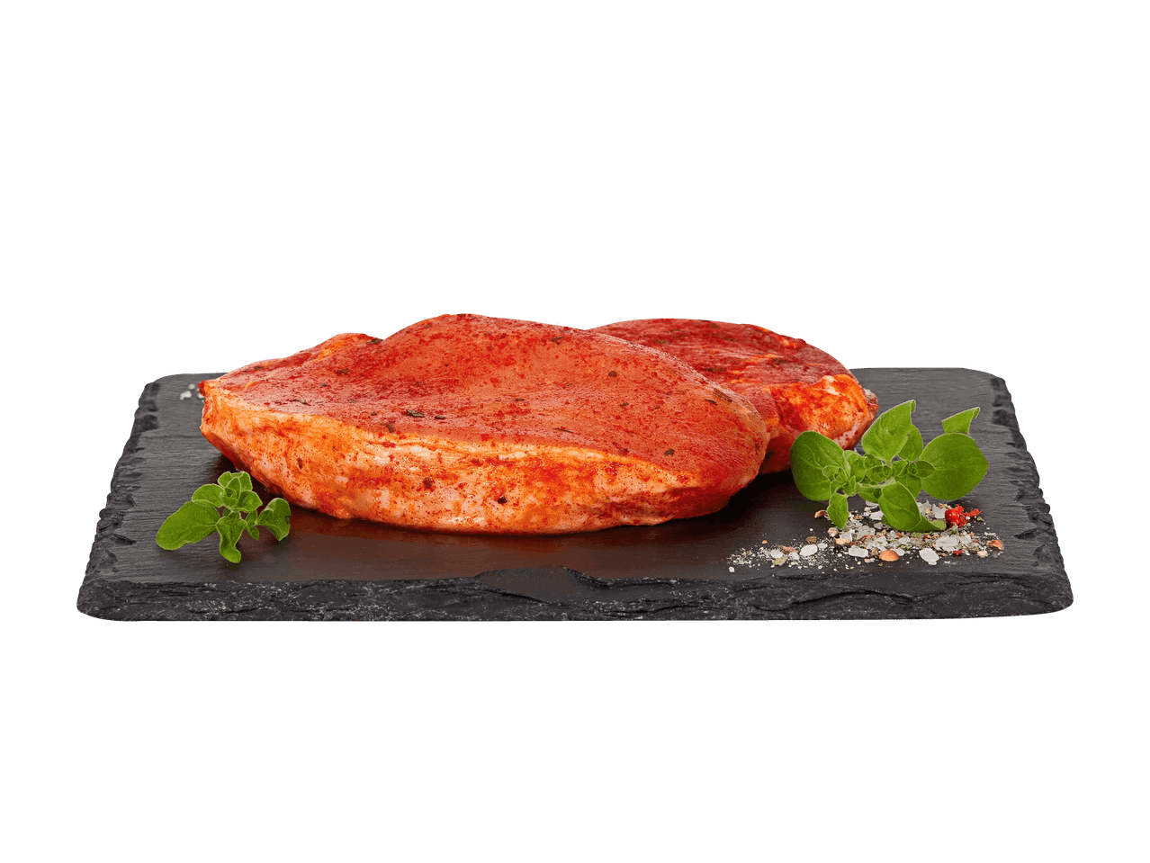 Zwei marinierte Schweinesteaks auf einem Schieferbrett mit Kräutern und Gewürzen.