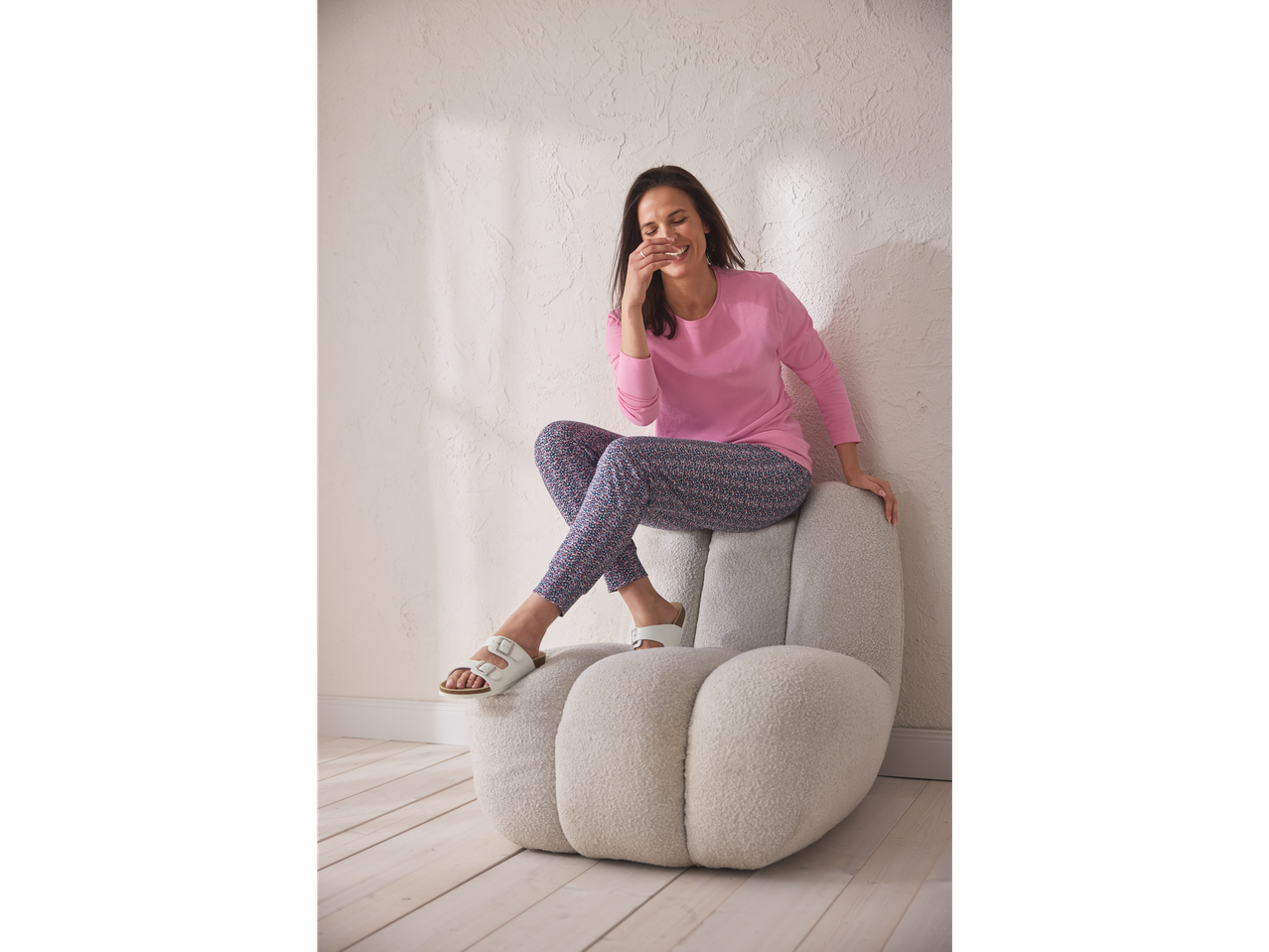Bljije vrouw in roze Esmara pyjama en bedrukte broek zit op een stoel.