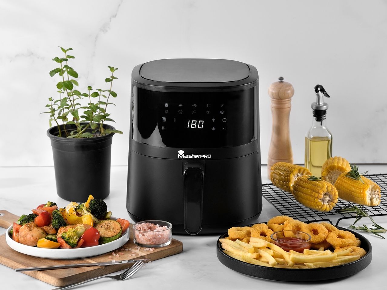 Una friggitrice ad aria nera MasterPRO su un tavolo con verdure, patatine fritte e pannocchie.