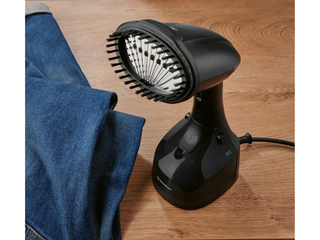 Silvercrest handheld garment steamer with brush attachment next to blue jeans on a wooden surface.