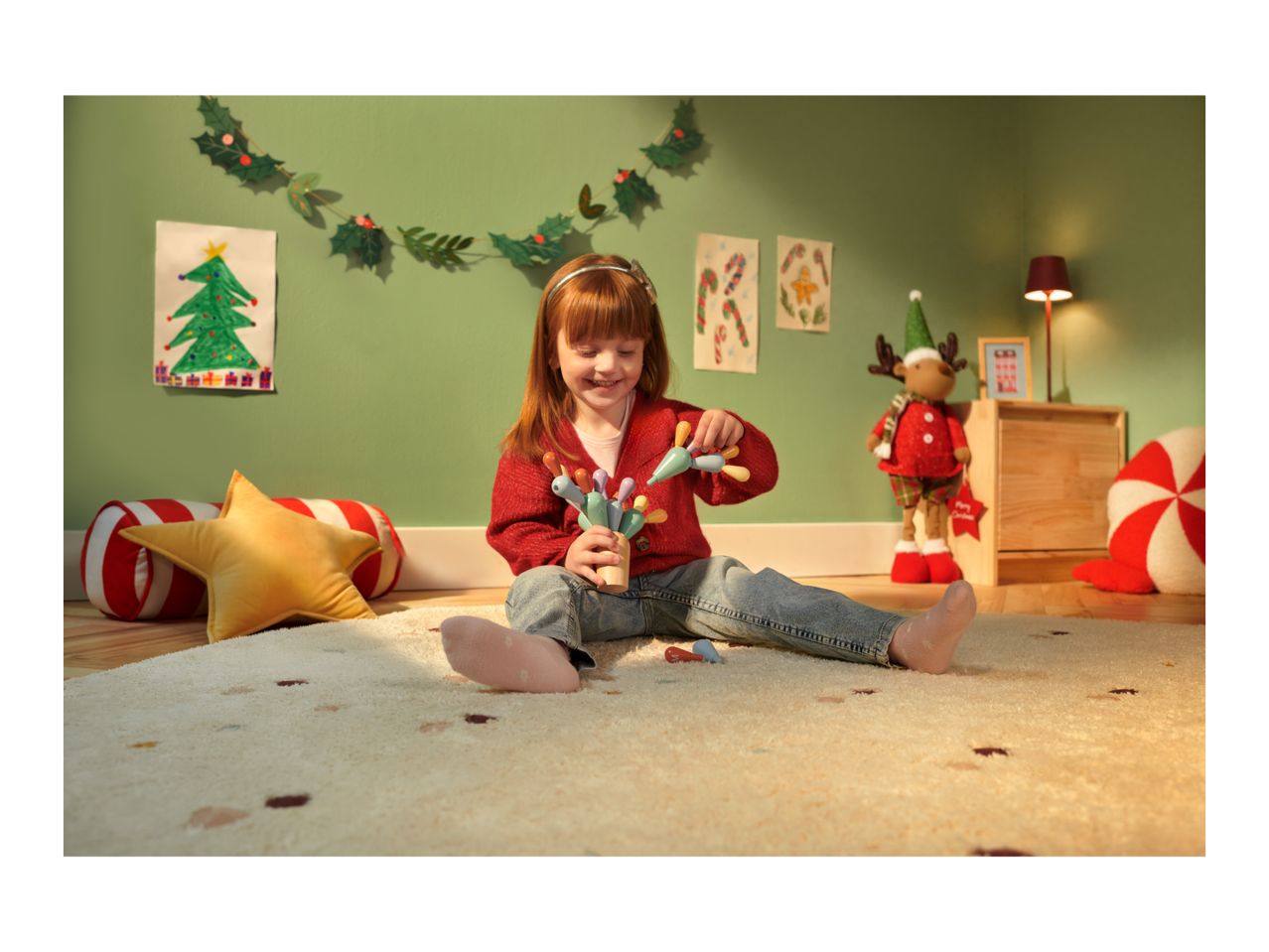 A girl playing with wooden toys on a rug in a Christmas-decorated room.