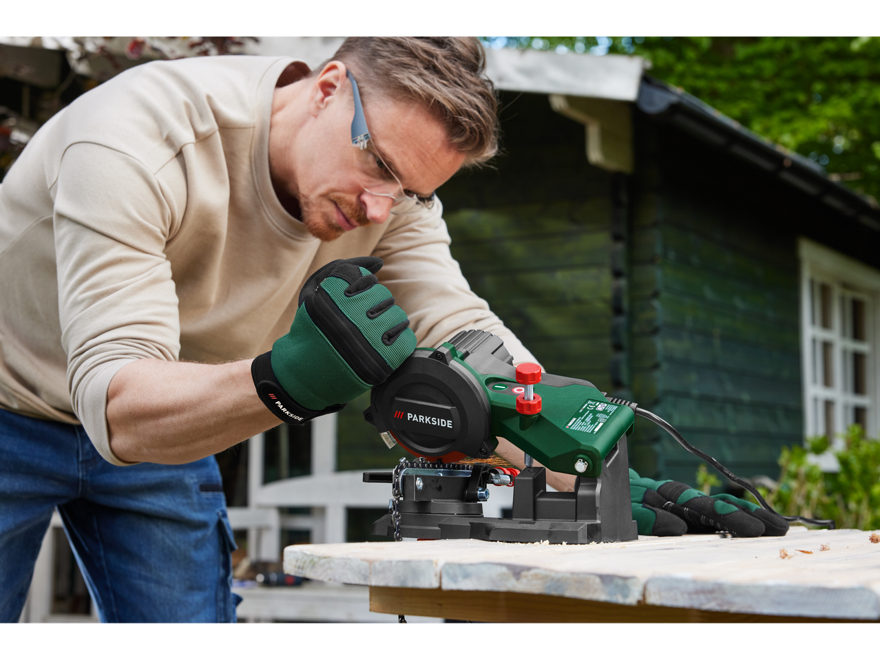 A man uses a Parkside chainsaw sharpener outdoors.