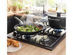 A black frying pan and pot simmer on a gas stovetop, cooking broccoli and chicken.