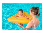 Smiling baby in a yellow inflatable boat with a woman in a swimming pool.