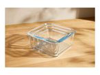 Three clear glass square food storage containers, nested, on a wooden surface with shadows.