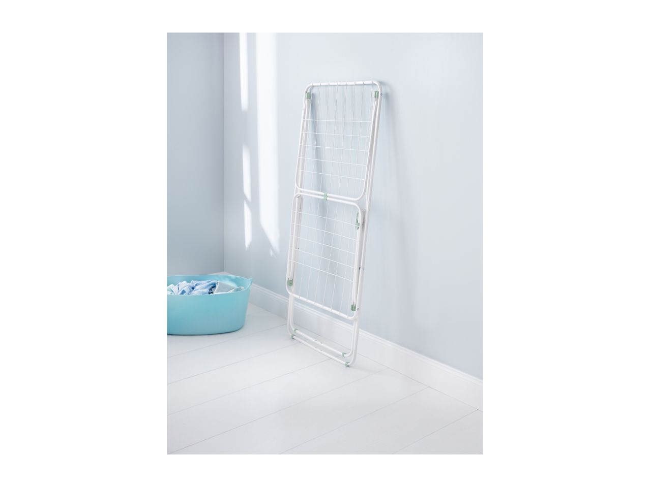 White clothes drying rack leaning against a light blue wall, with a laundry basket