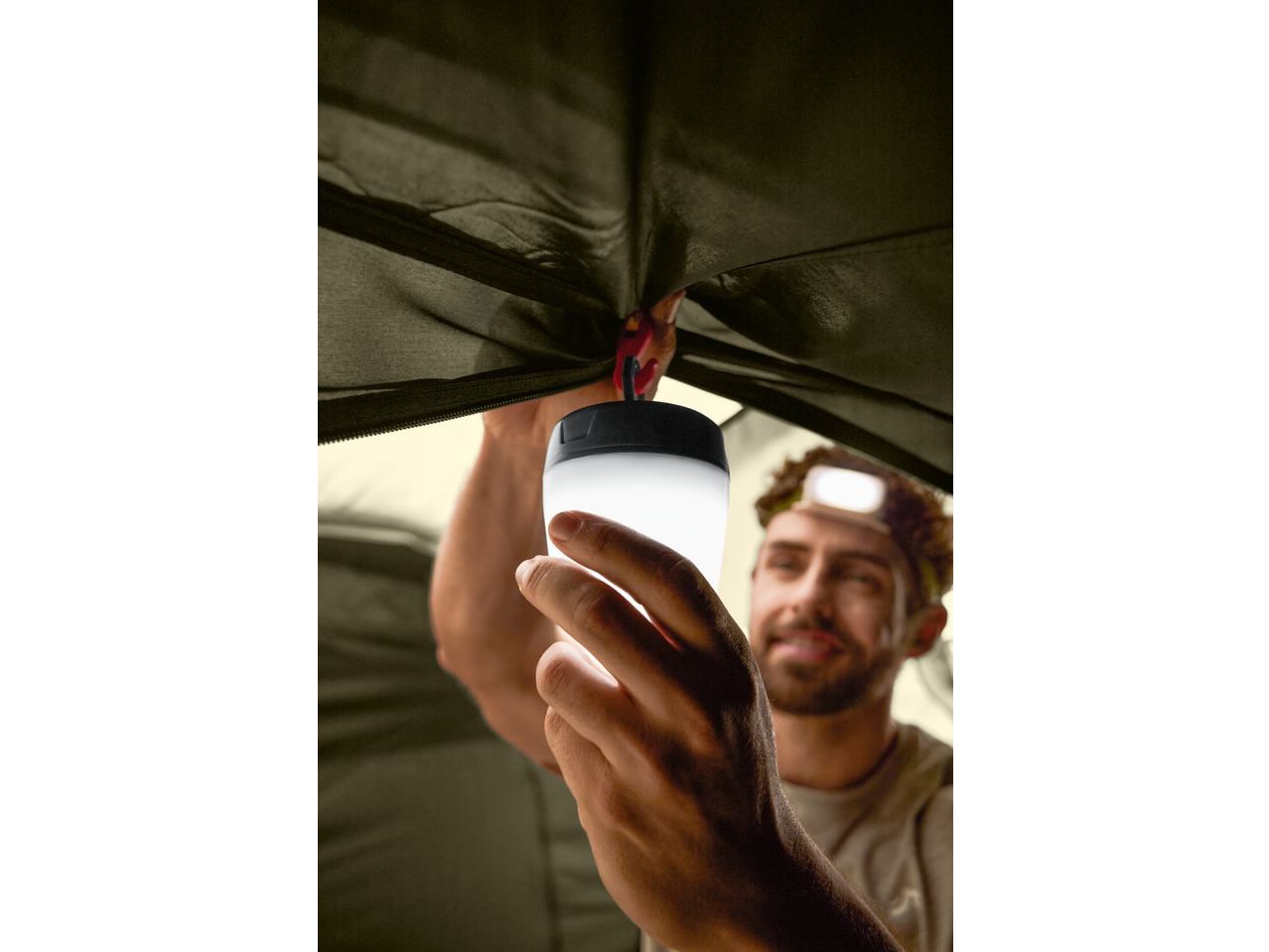 Bărbat agățând o lanternă de camping CRIVIT în interiorul unui cort.