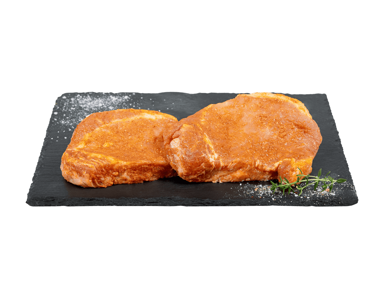 Due bistecche di maiale marinate su un tagliere di ardesia con sale e rosmarino.