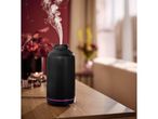 A black essential oil diffuser emitting steam on a wooden table.