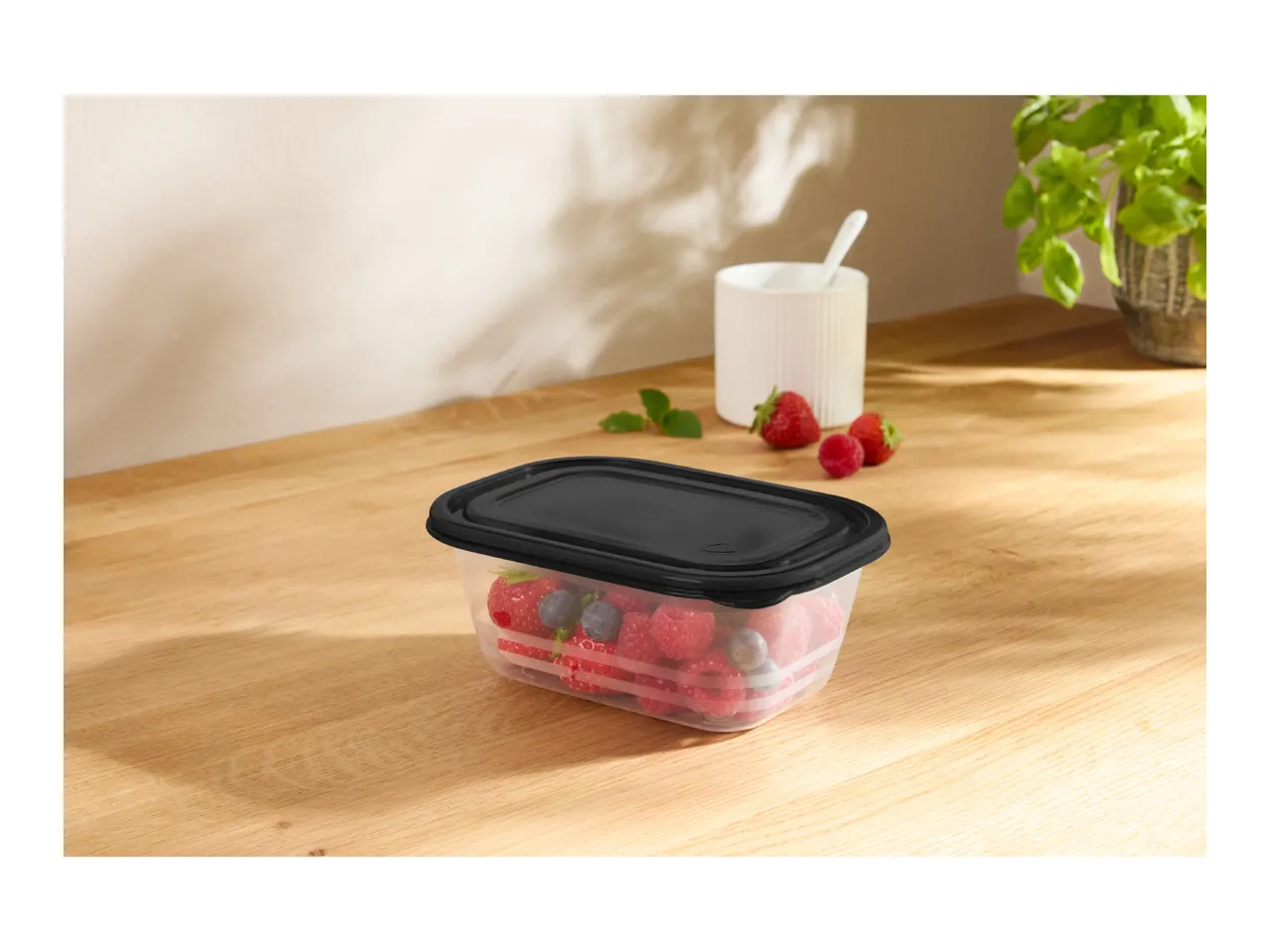 Clear food container with black lid filled with berries on a wooden table.