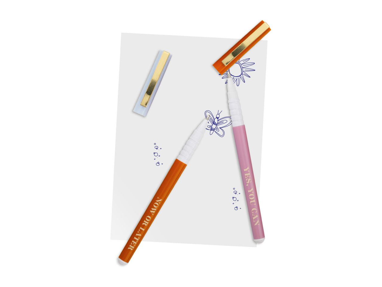 Two colorful pens, one orange with 'NOW OR LATER' and one pink with 'YES, YOU CAN', on a white paper with doodles.