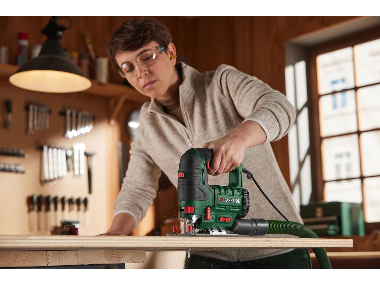 A woman uses a Parkside jigsaw to cut wood in a workshop.