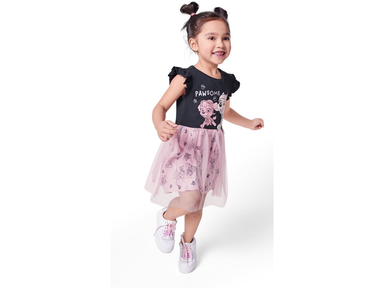 A girl joyfully leaps in a Paw Patrol-themed dress and white sneakers.