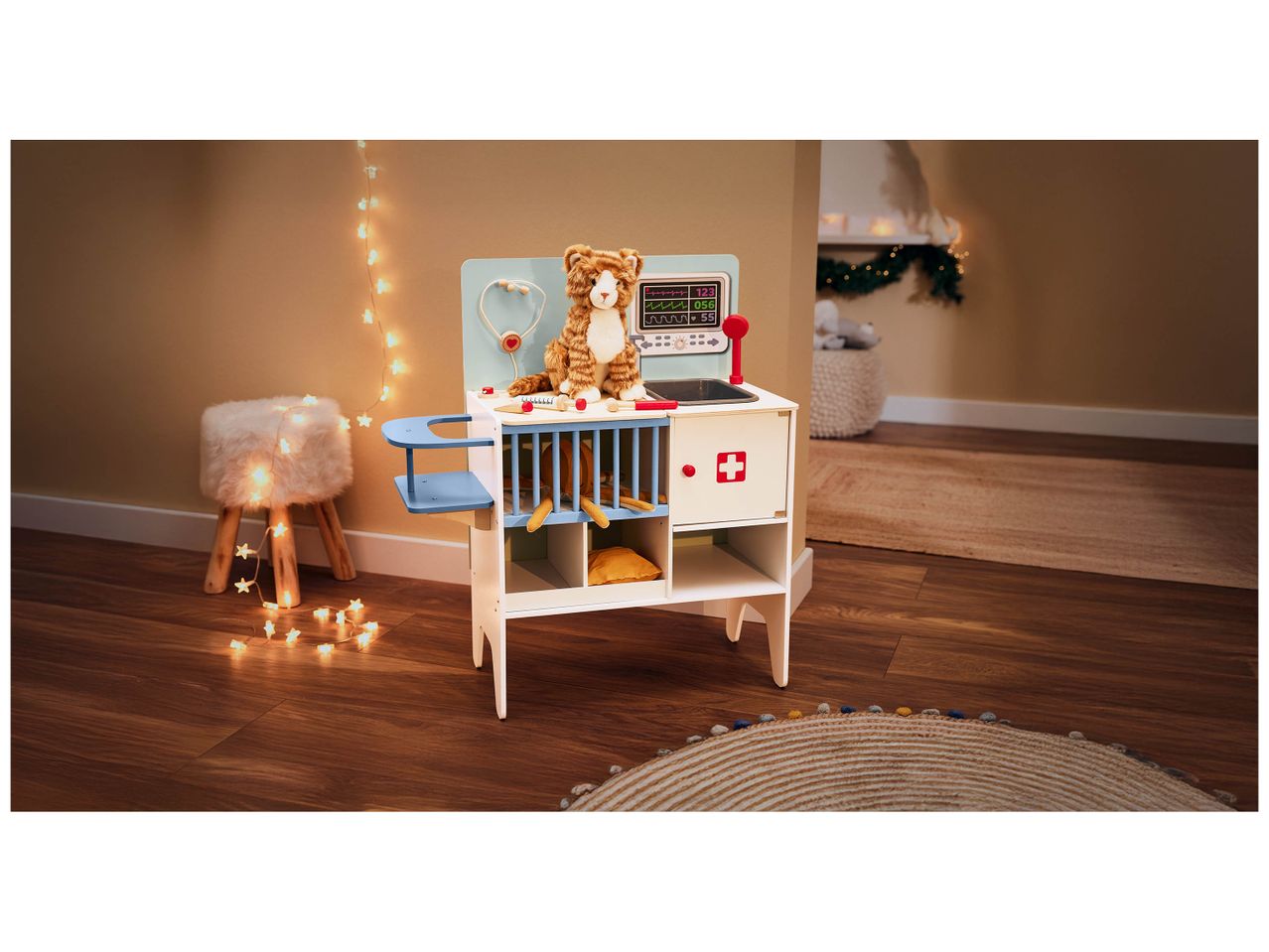 Un jouet de vétérinaire en bois avec un chat en peluche, un stéthoscope et un moniteur, entouré de lumières étoilées.