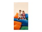 Two children in tracksuits sitting on colorful cushions, smiling and playing.