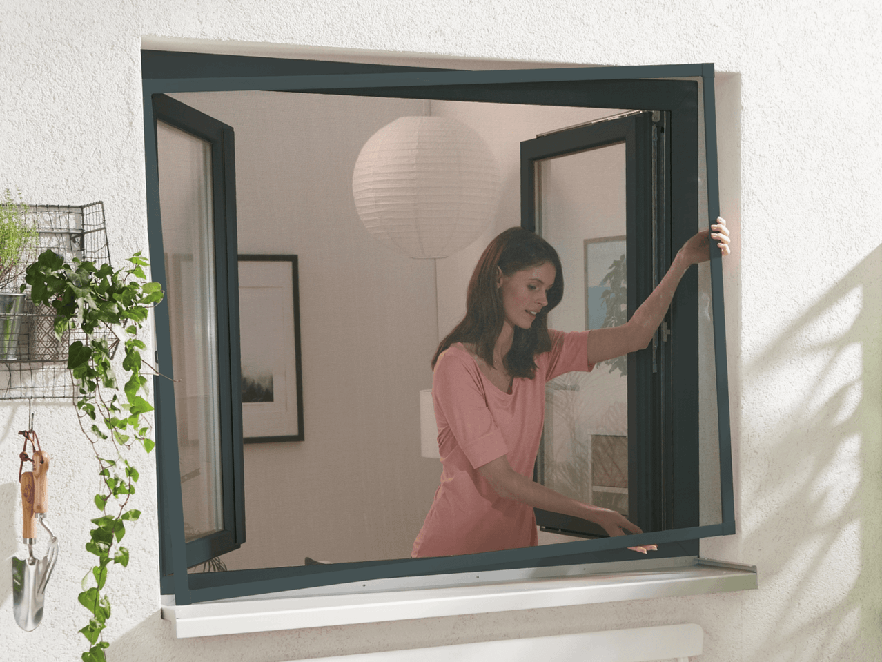 Frau öffnet ein Insektenschutzfenster mit integriertem Rollo.