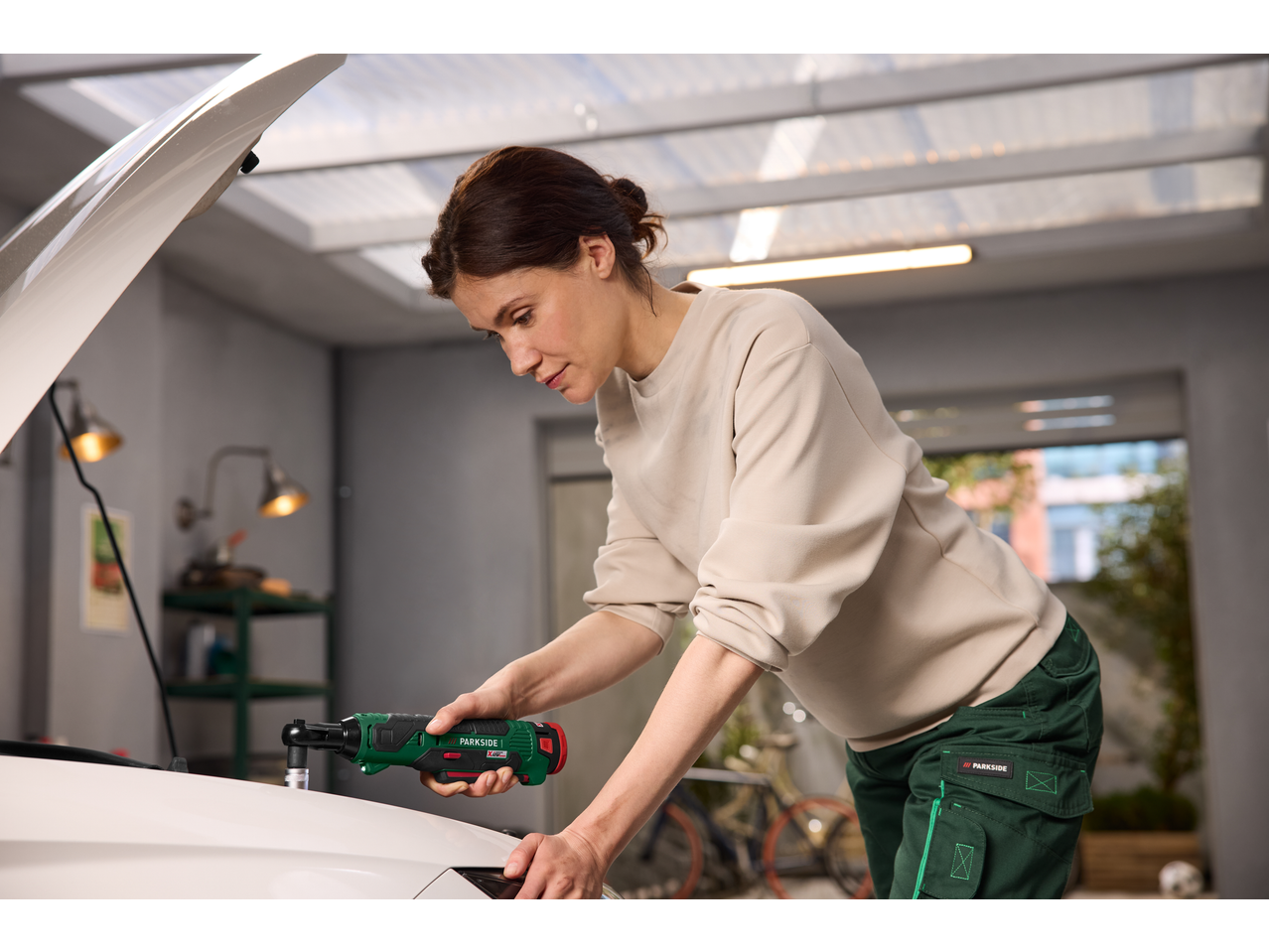 Woman using a PARKSIDE cordless ratchet wrench to repair a car.