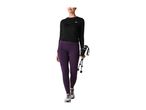 A woman walking in purple leggings and a black long-sleeved shirt, holding trekking poles.
