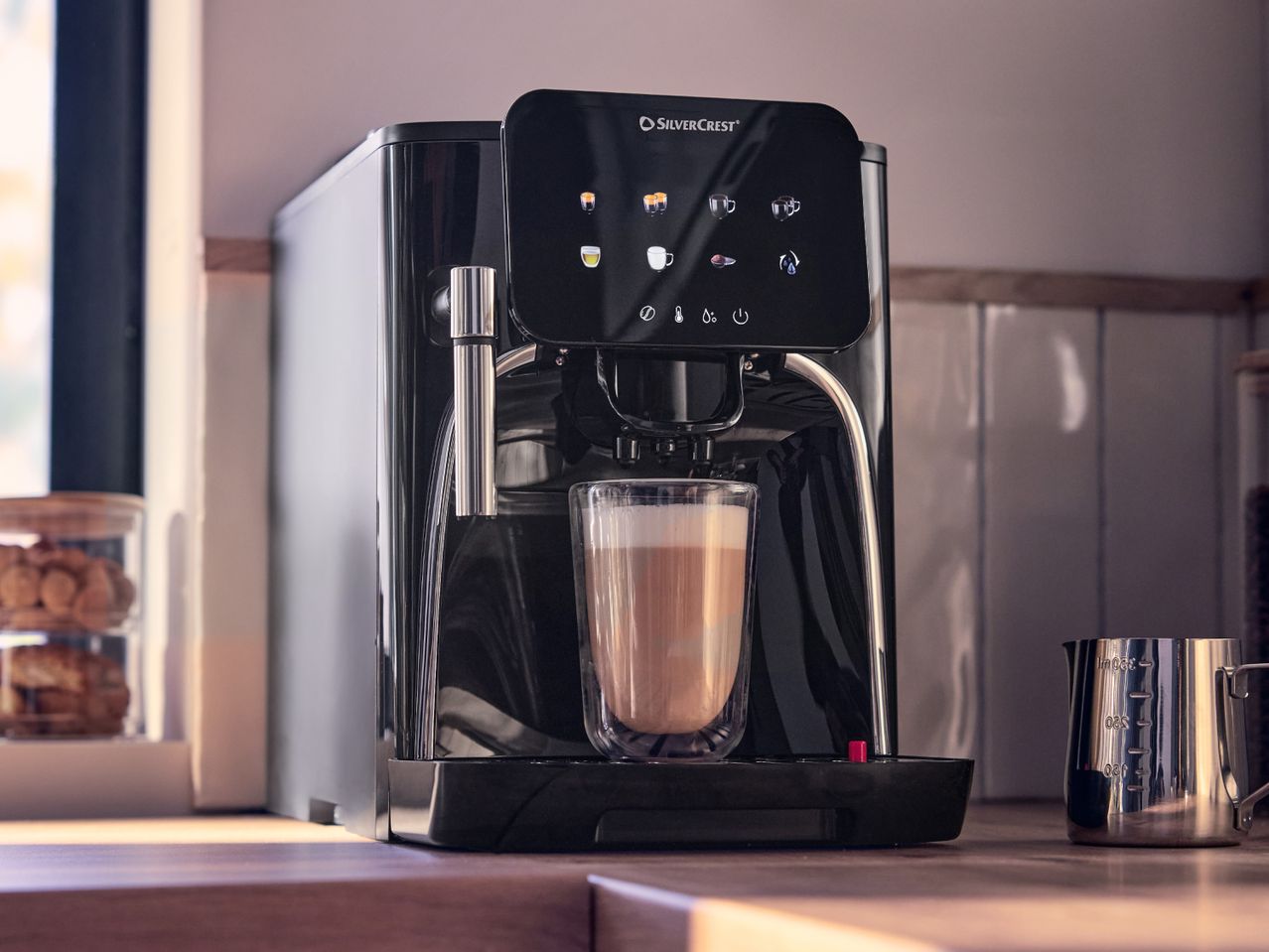 Automatic coffee machine with a latte in a glass, on a kitchen counter.