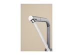 Chrome kitchen faucet with water flowing out, against a light beige background.