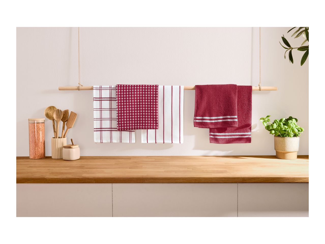 Assorted red and white kitchen towels hanging on a wooden rod above a countertop