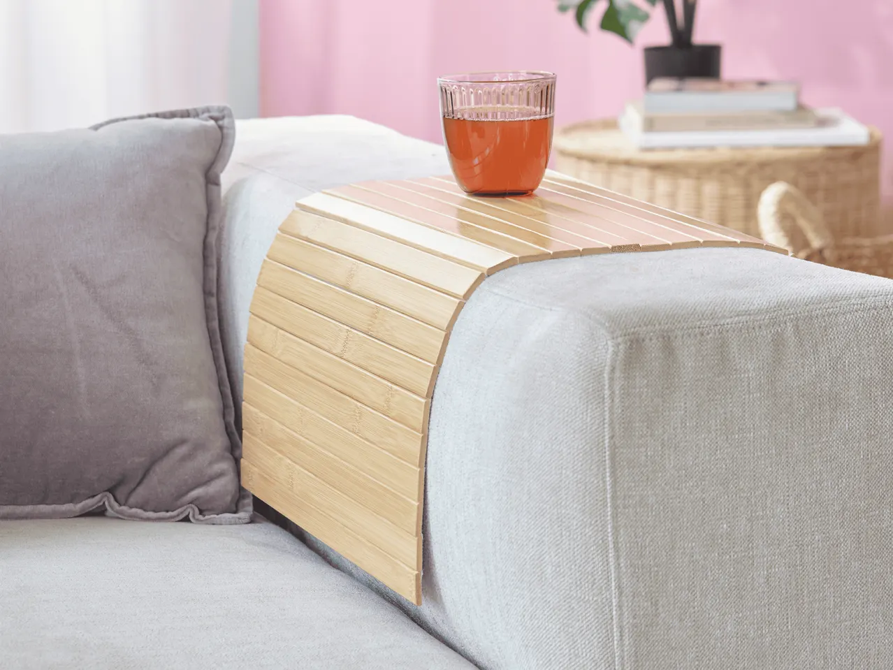 Bambus-Sofatablett mit einem Glas Getränk auf einem hellgrauen Sofa.