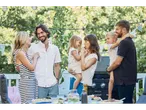 Uma família desfruta de um churrasco Grillmeister num jardim ensolarado.