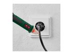 A green voltage tester with a red light is checking a black cable plugged into a white outlet.