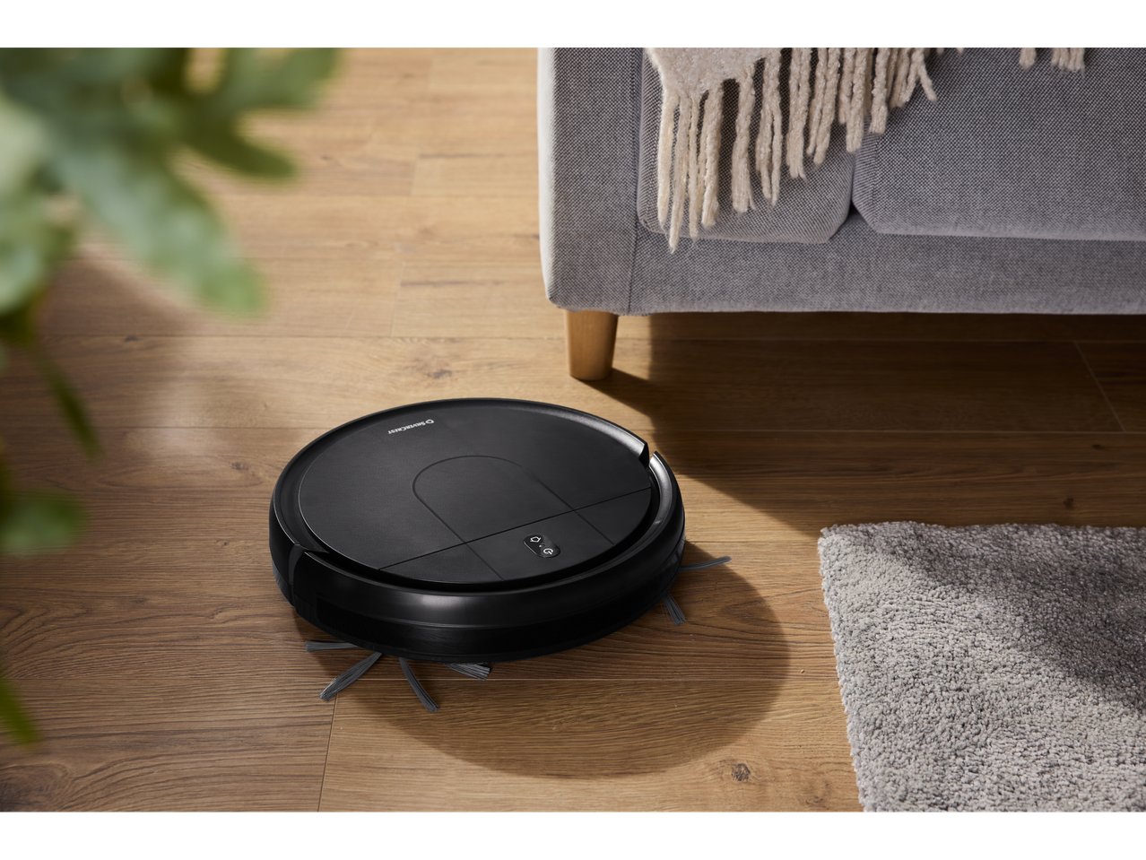 SILVERCREST® Robot Vacuum Cleaner on a wooden floor next to a sofa and rug.