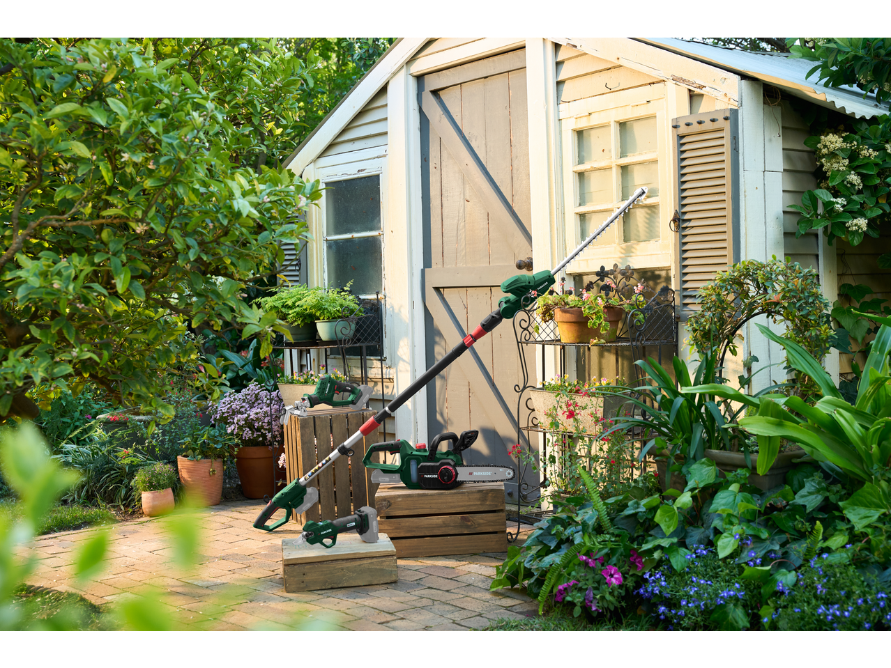 Serra de poda, corta-sebes e motosserra a bateria PARKSIDE num barracão de jardim.