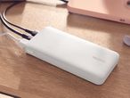 White power bank charging on a wooden surface, with a pink phone in the background.