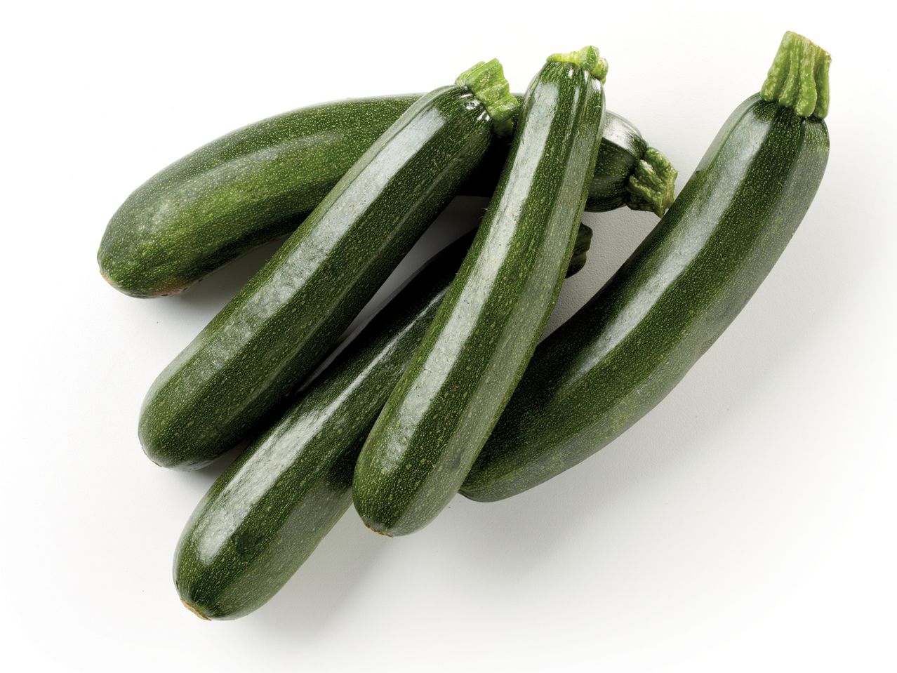 Zucchine verdi fresche disposte su sfondo bianco.