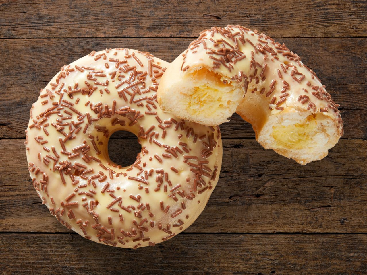 Ein glasierter Donut mit Dekor, teilweise angeschnitten, auf Holz.