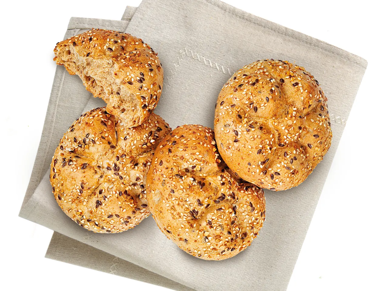 Vollkornbrötchen mit Sesam und verschiedenen Körnern auf einem Leinen-Tischtuch.
