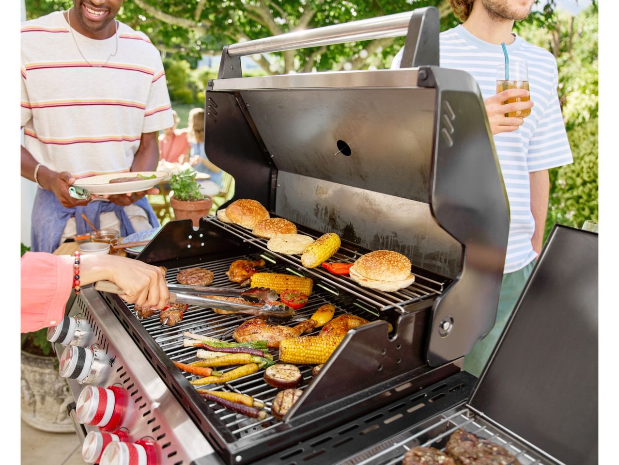 People grilling burgers, chicken, corn, and vegetables on a barbecue in a garden.