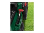 Close-up of a green lawnmower with a red height adjustment lever on green grass.